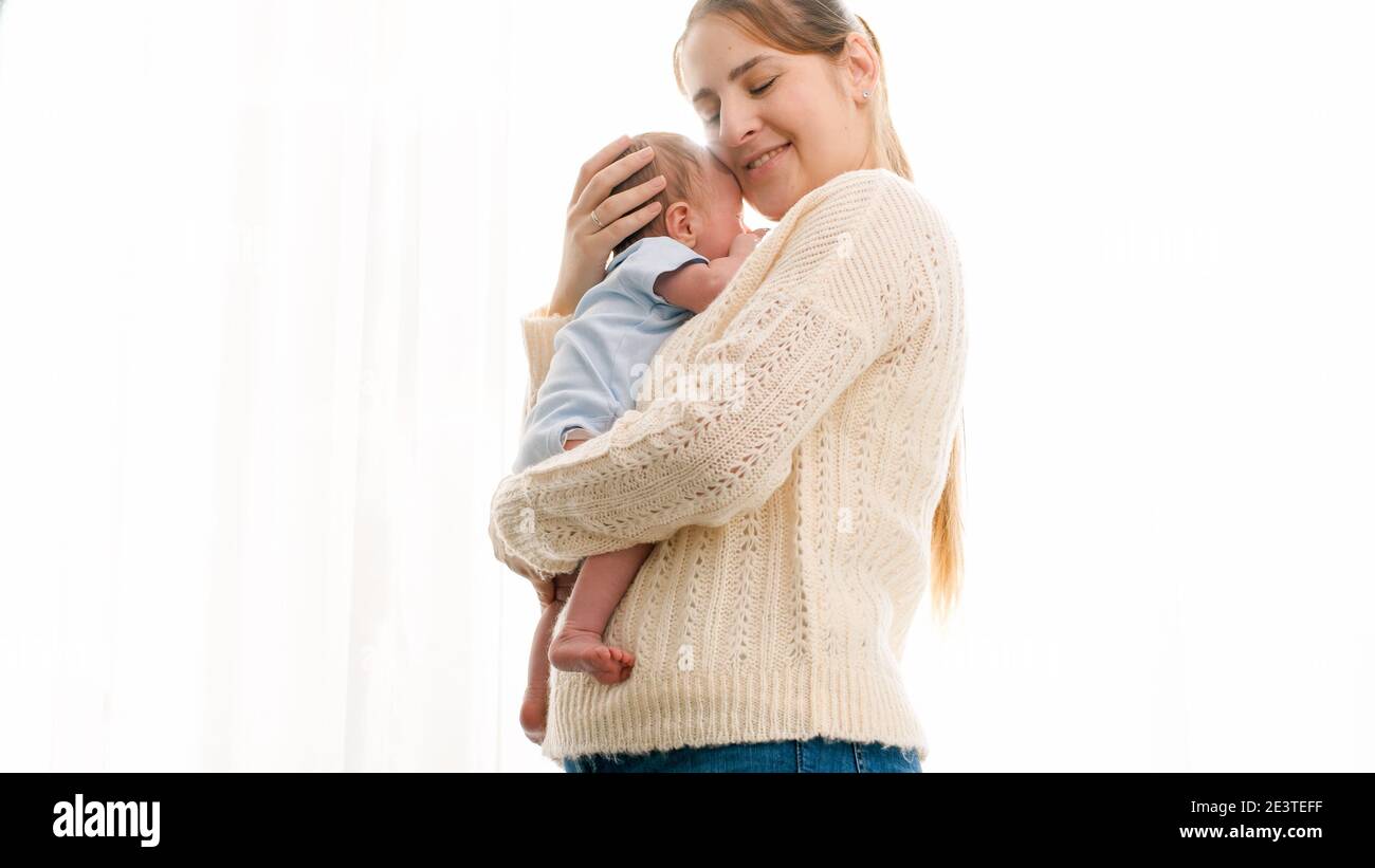 Portrait of mother cuddling newborn baby in sun light shining through ...