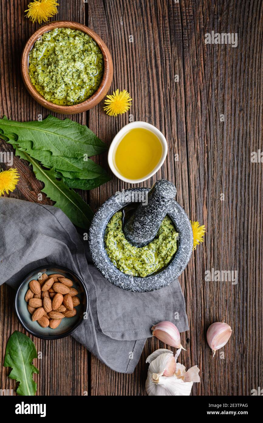 Healthy dandelion pesto with almonds, garlic, olive oil and Parmesan cheese in a stone mortar on rustic wooden background Stock Photo