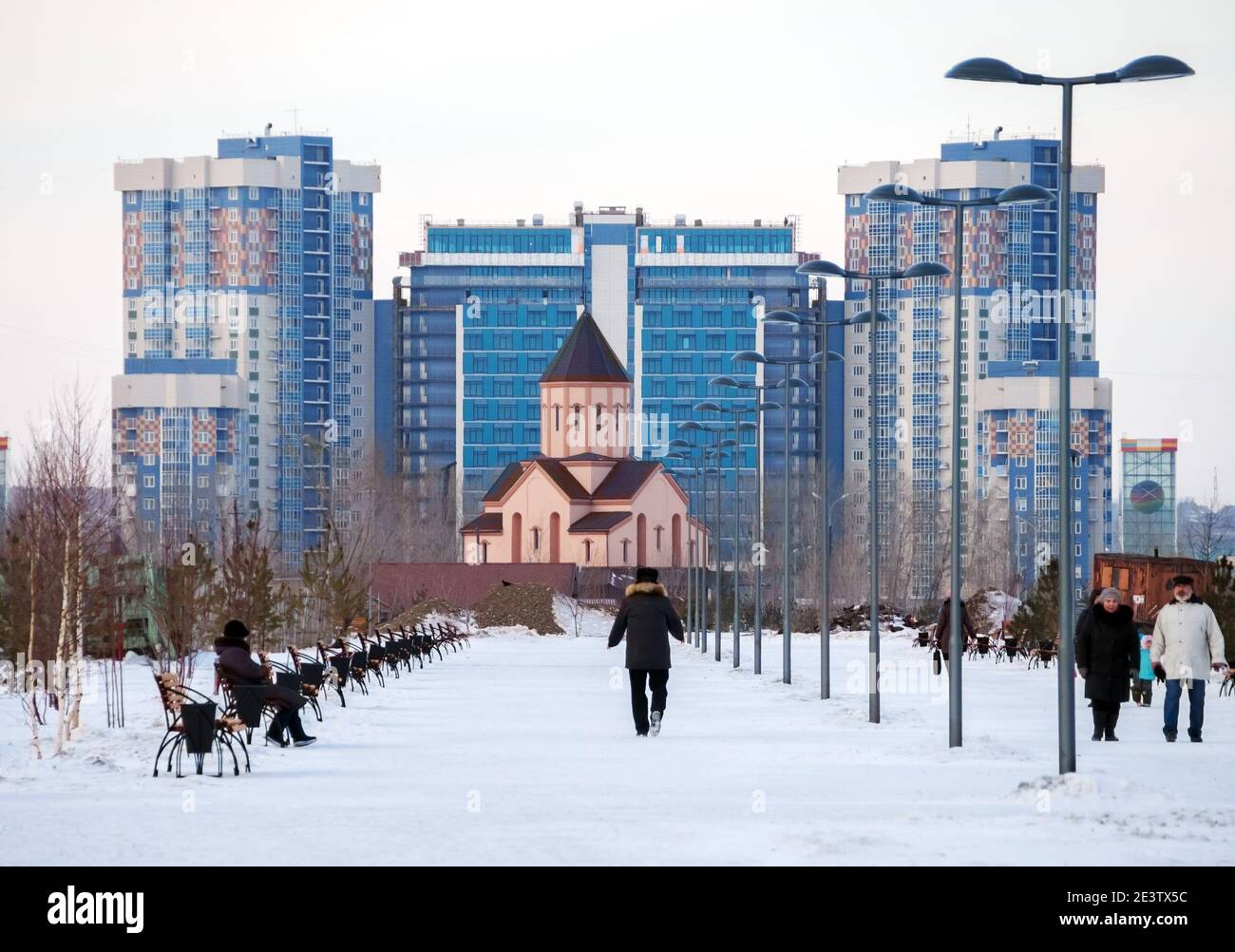 People are resting in the park against the background of the Armenian Church and residential buildings on a cloudy winter evening. Stock Photo