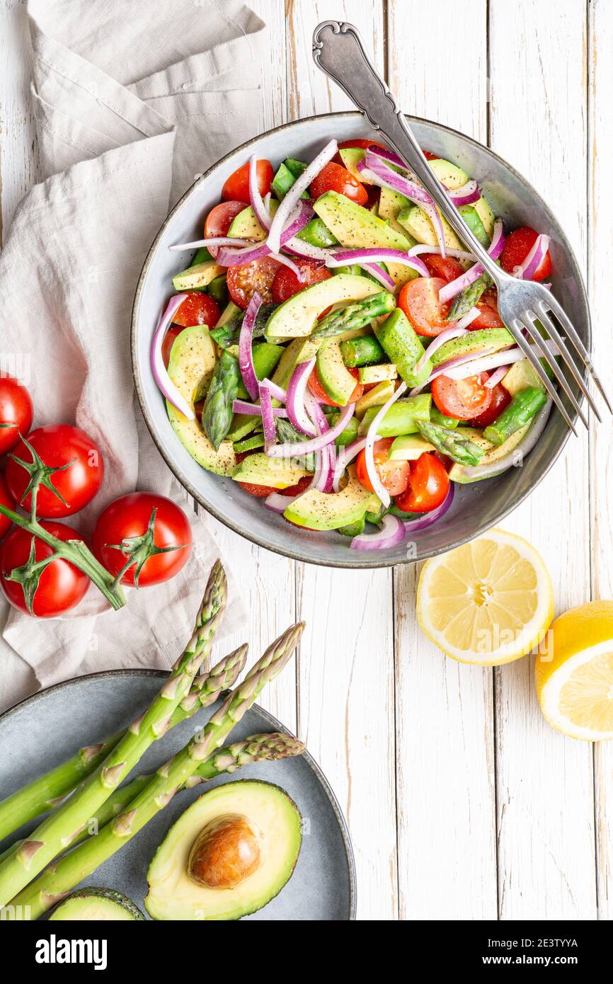 Healthy vegan meal, Juicy summer salad with blanched asparagus, cherry tomatoes, avocado slices and red onion, sprinkled with pepper and drizzled with Stock Photo