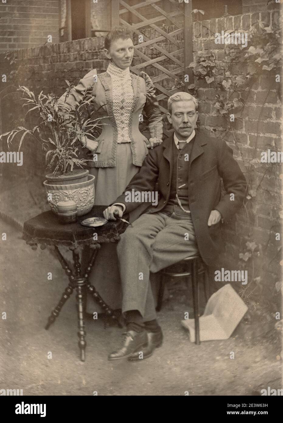 Affectionate home photo of 1890s Victorian unknown fashionably dressed mature man and transgender cross dressed partner in a garden. One of a sequence of ten photographs of friends and family in the same setting. Stock Photo