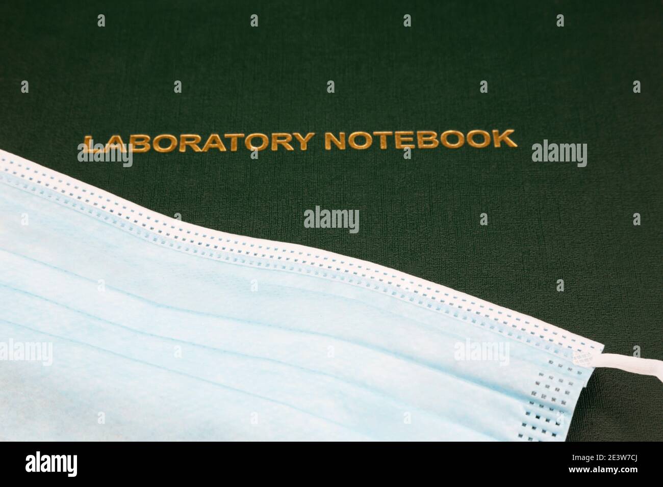 Medical protection of face mask placed on green Laboratory Notebook reflects data based processes applied to infectious disease treatment and studies Stock Photo