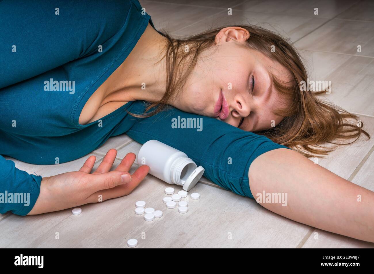 Woman committing suicide with pills - depression woman lying on the floor at home after an overdose of pills Stock Photo