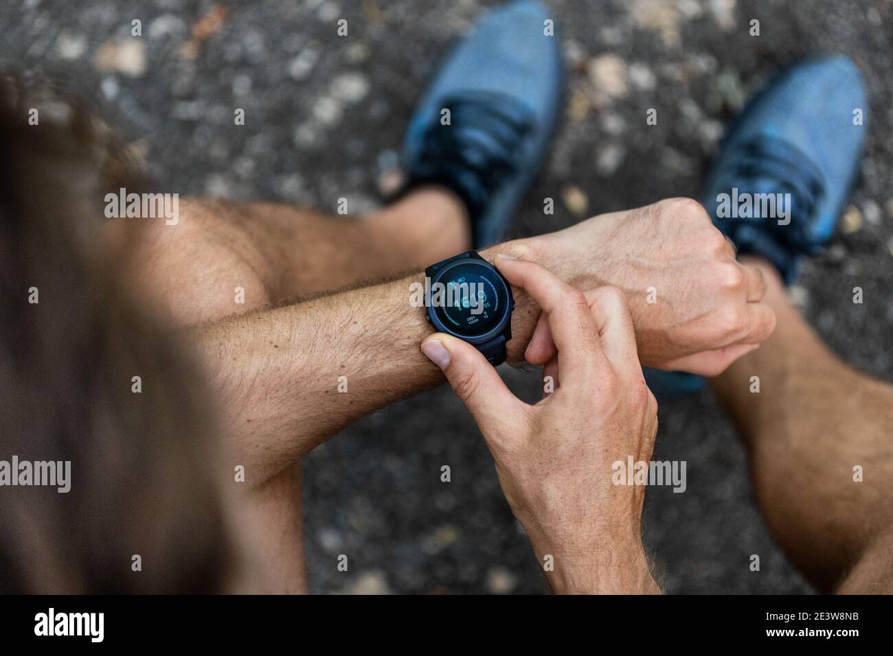 Fit man checking smart watch wearable technology sport smartwatch on fitness run walk outside. Top view from above with running shoes in street. Stock Photo