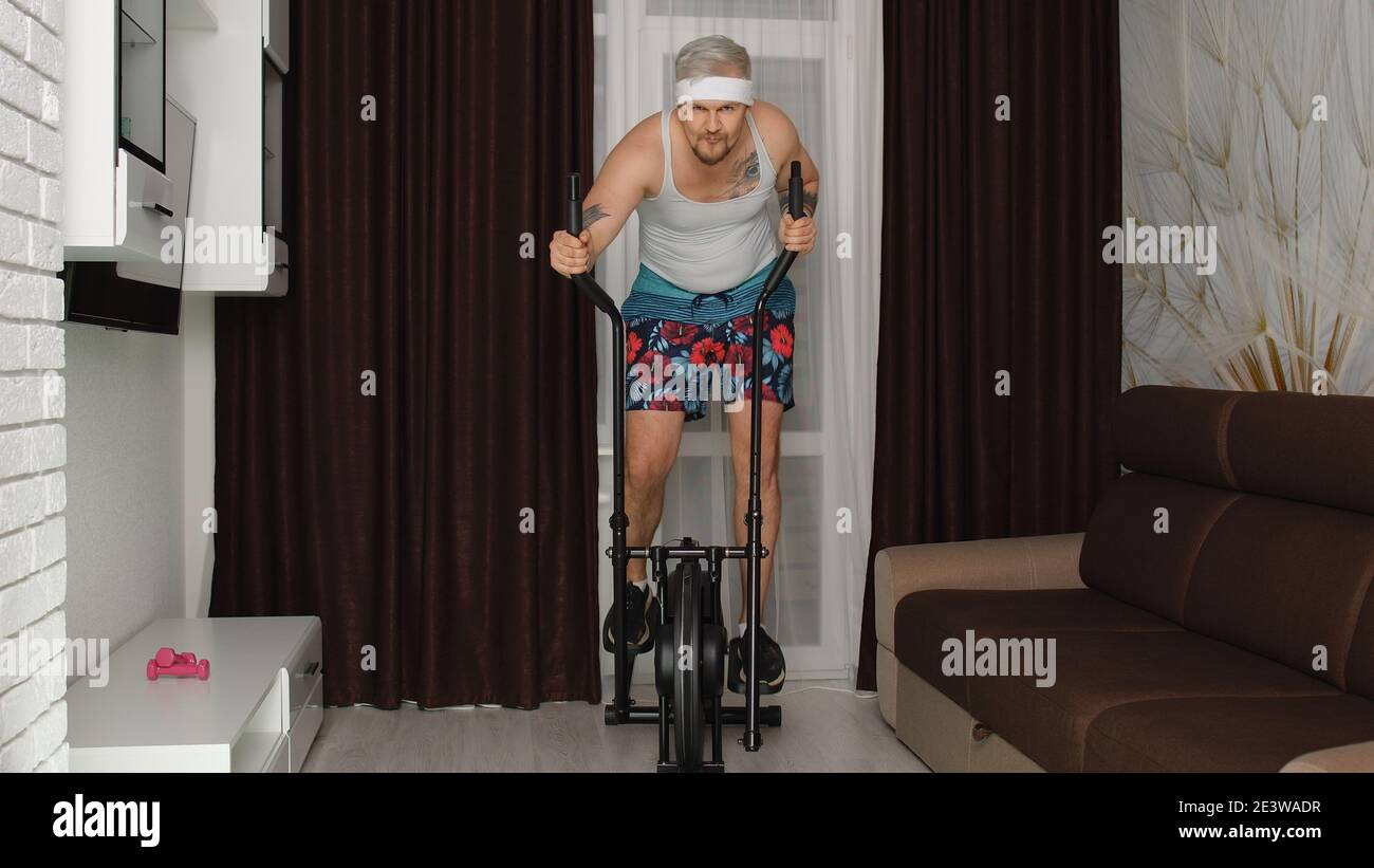 Funny Caucasian athlete sportsman guy couch on orbitrek in living room