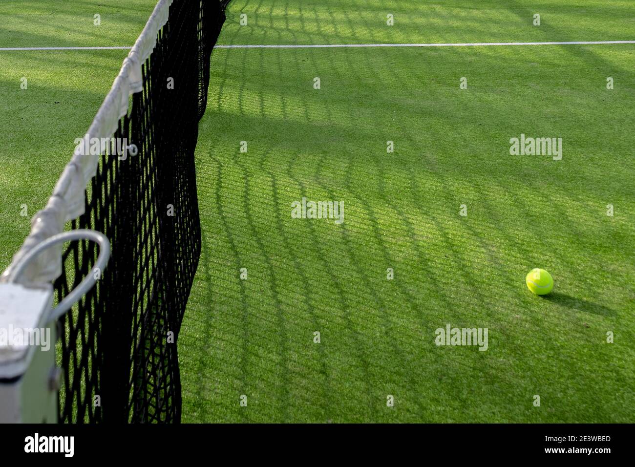 Selective focus of a black net with white protection to play paddle or tennis and a ball from the same game on green artificial grass with copy space Stock Photo
