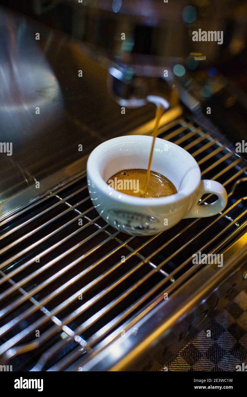 Fresh espresso dripping from portafilter of coffee machine into white cup Stock Photo