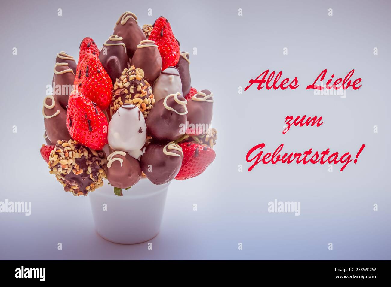 Happy birthday greeting card in German Language with red lettering that reads Alles Liebe zum Geburtstag; A bunch of edible flowers, arrangement of ch Stock Photo
