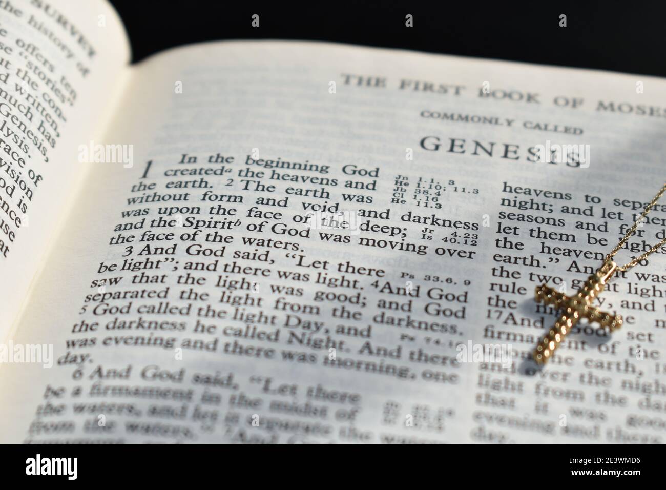 Closeup of the first book of the Bible with a gold cross laying on the page. Genesis Chapter 1, verse 1. In the beginning God said Stock Photo
