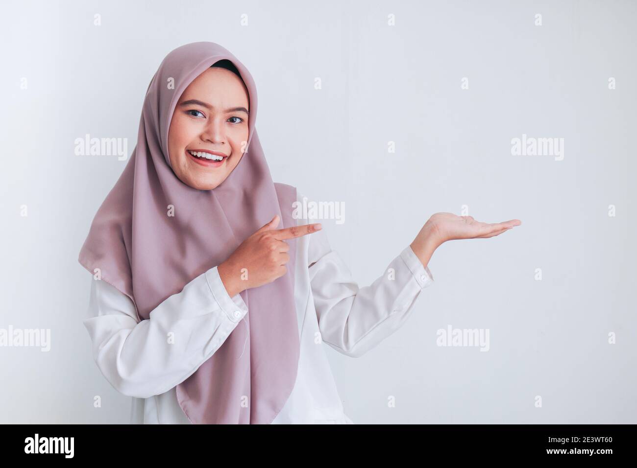 Asian Islam Muslim woman wearing headscarf is pointing finger to blank copy space smile face area. Indonesian woman. Religion concept isolated on gray Stock Photo