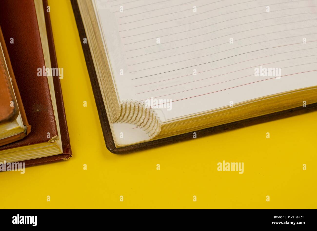 Close-up of old diaries on yellow background. Two closed diaries and one open one with the special corners torn off at the bottom of the pages. Stock Photo