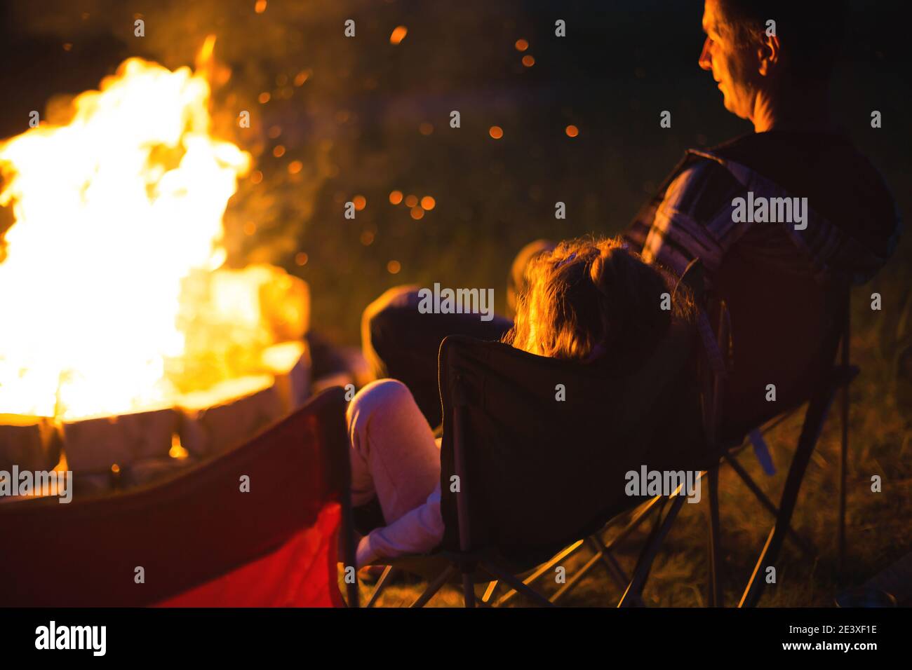 Dad and daughter sit at night by the fire in the open air in the summer
