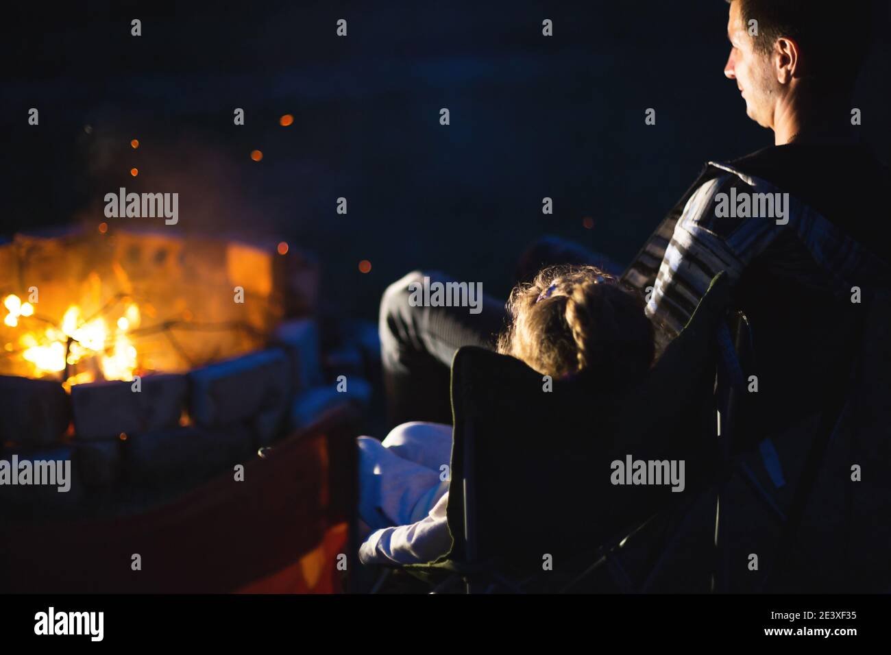 Dad and daughter sit at night by the fire in the open air in the summer
