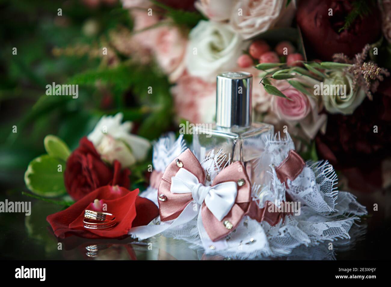 Wedding accessories for the bride and groom: a bouquet of red, pink and white roses, a boutonniere, gold wedding rings, a lace garter with a bow, perf Stock Photo