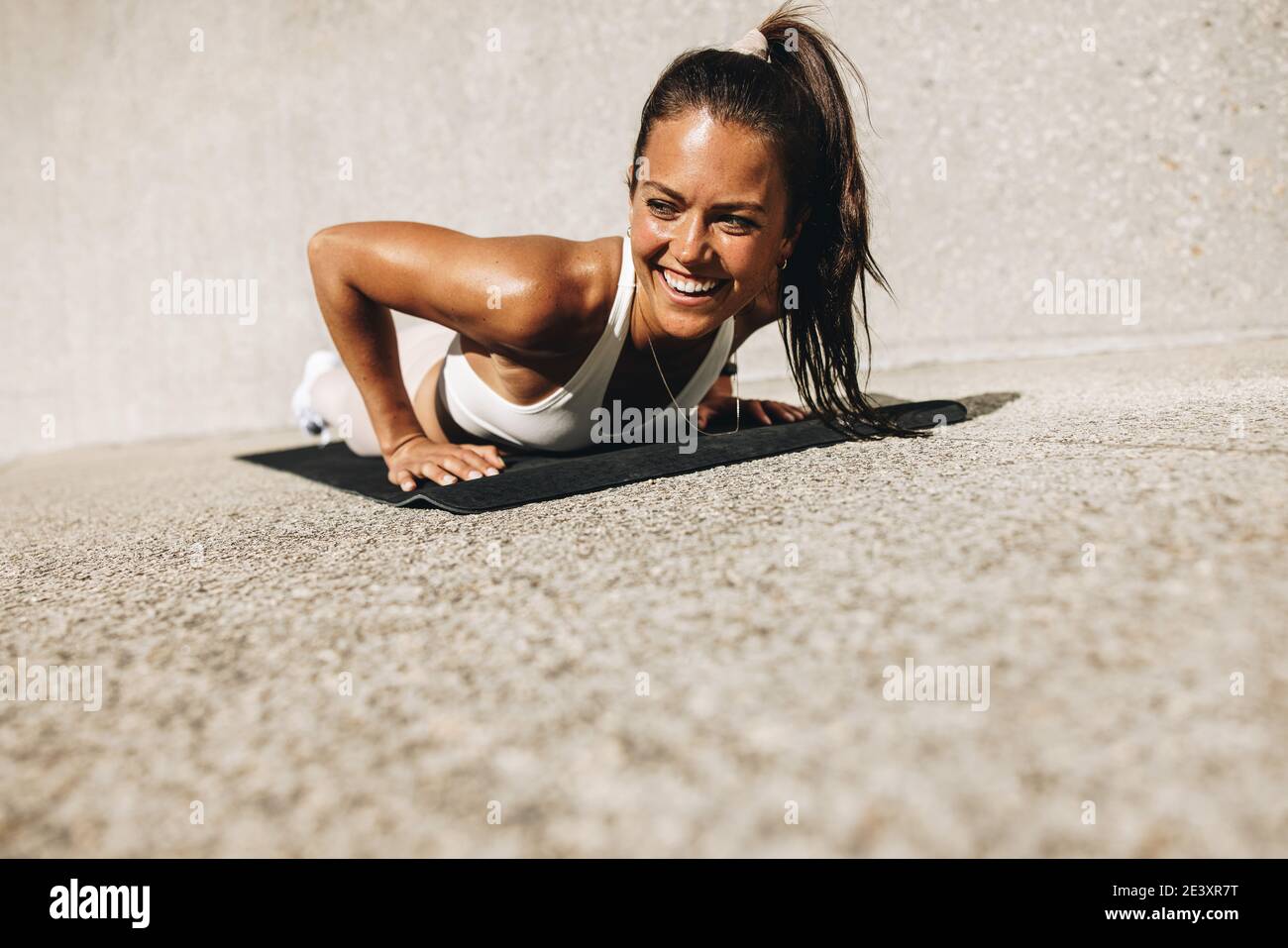 Woman doing push ups on exercise mat. Female in sportswear smiling during her workout. Stock Photo
