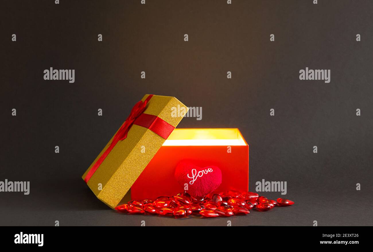 Open red gift box with a bow with a golden glow and glitter inside on a ...