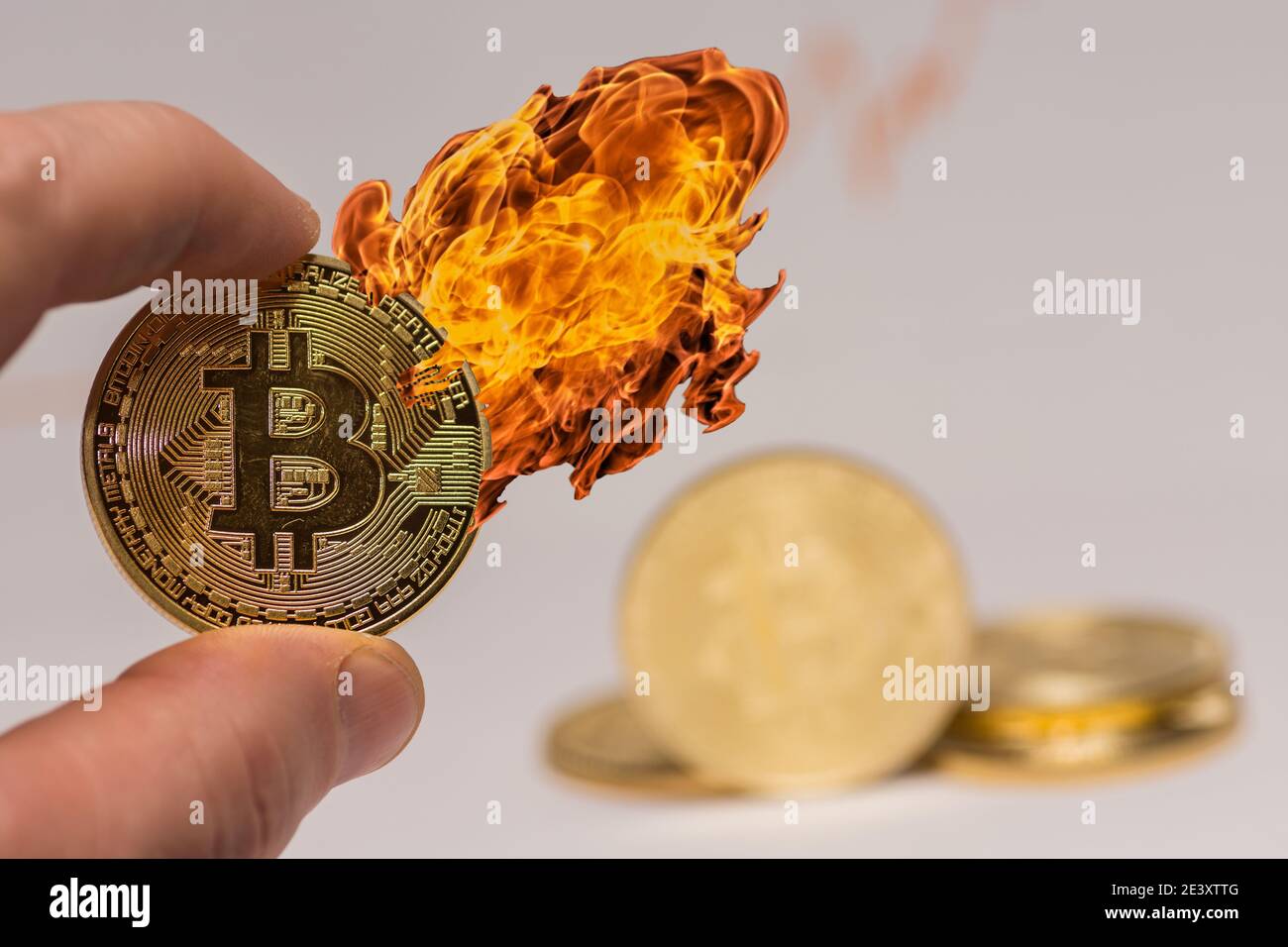 bitcoin held between two fingers with hot fire on the coin with other coins in the background Stock Photo