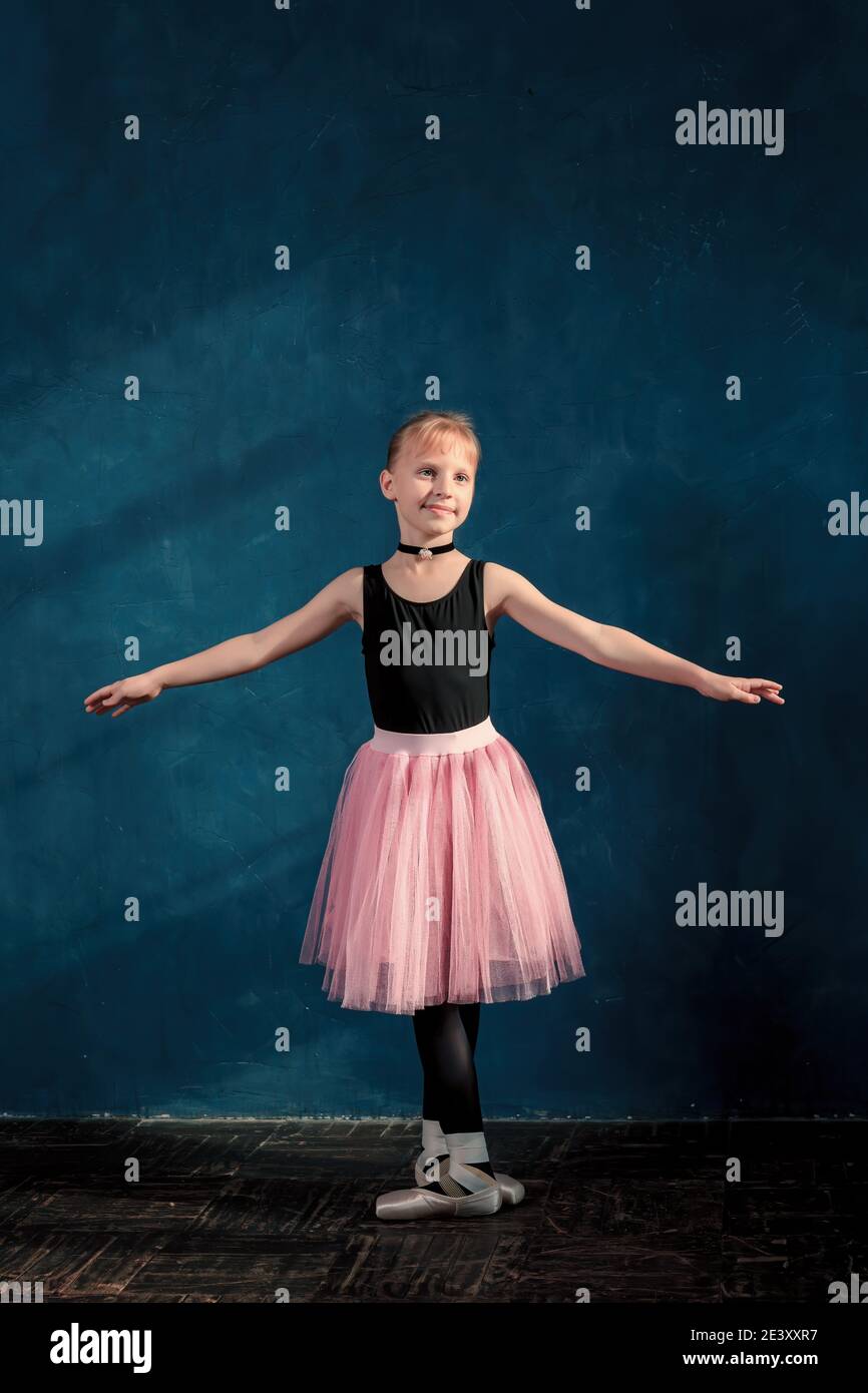 Cute little girl in pink tutu and pointe shoes training ballet position against wall in studio class Stock Photo