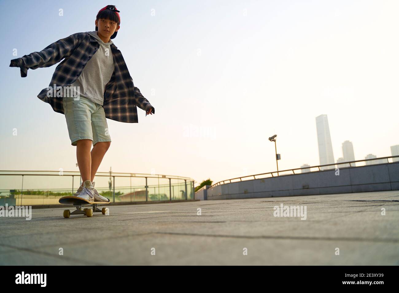 teenage asian child skateboarding outdoors on a pedestrian bridge Stock Photo