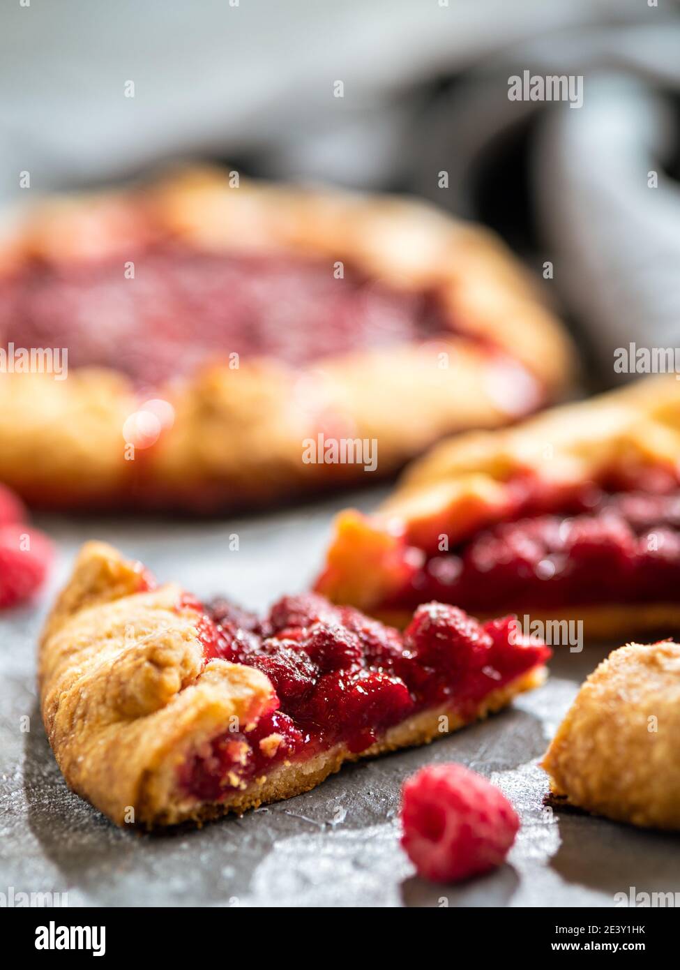 Slice of perfect raspberry galette. Delicious rustic homemade tart with frozen or fresh raspberries on gray background. Beautiful piece of galette with raspberries, copy space. Vertical Stock Photo
