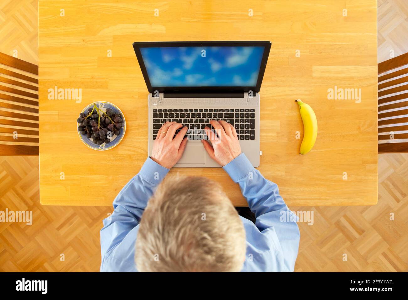 Businessman working in home office with laptop and fruits on a wooden table - overhead view Stock Photo