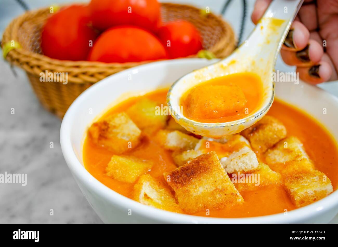 Closeup of human hand taking Tomato Soup with bread croutons in a soup spoon Stock Photo