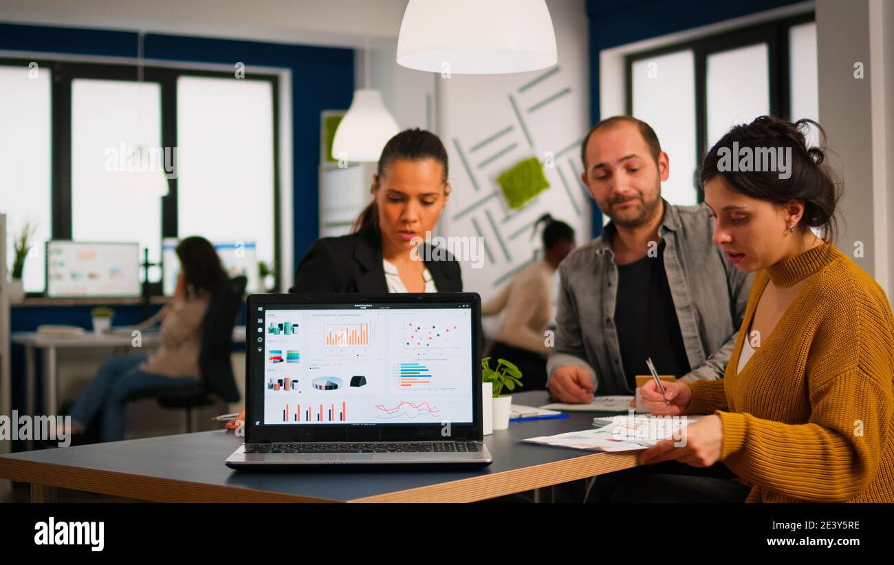 Team of colleagues employees cooperating sitting at desk in startup company office analysing graphs, taking notes. Business coworkers planning start up business project, brainstorming in wokrplace Stock Photo