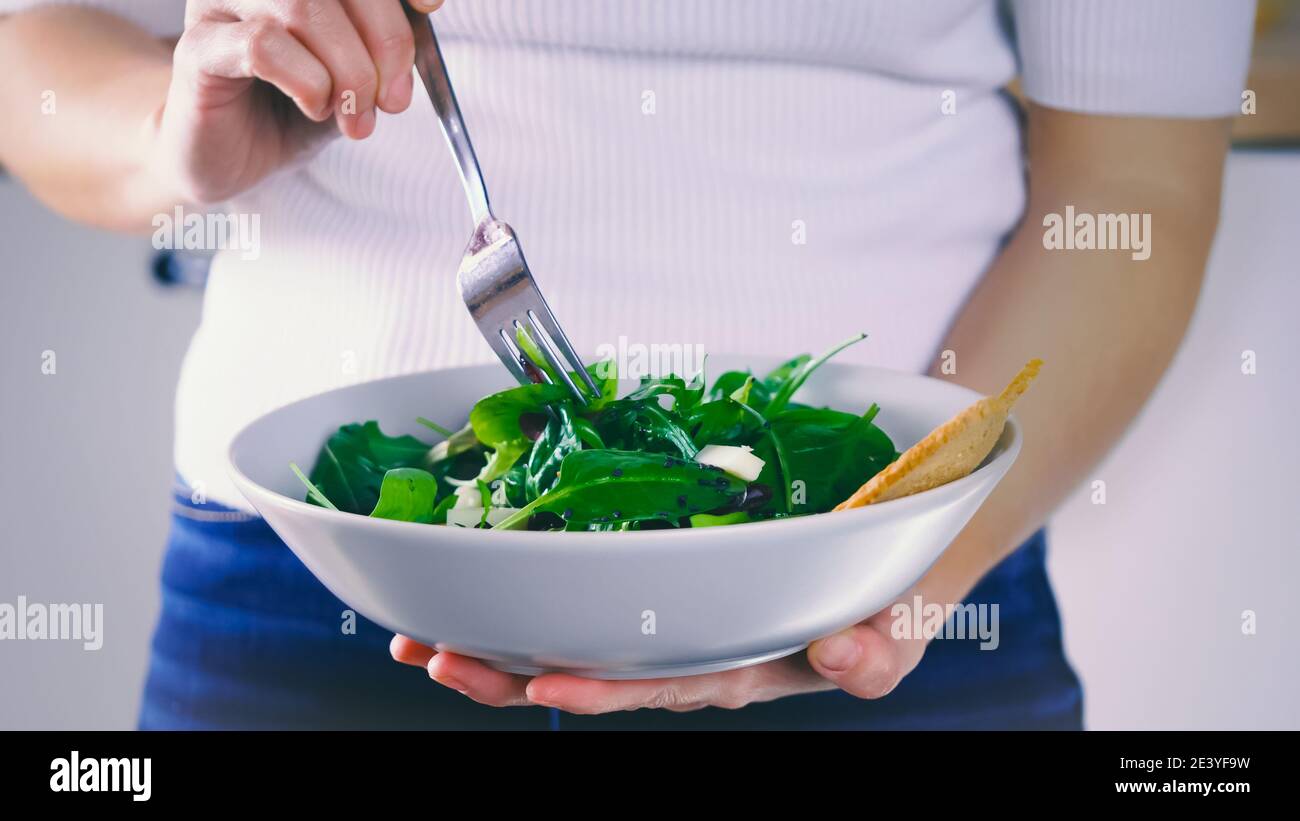 Eating salad, woman standing eats a meal of salad. Fresh and light lunch. Organic vegetable, natural ingredients for healthy nutrition. Eating green f Stock Photo