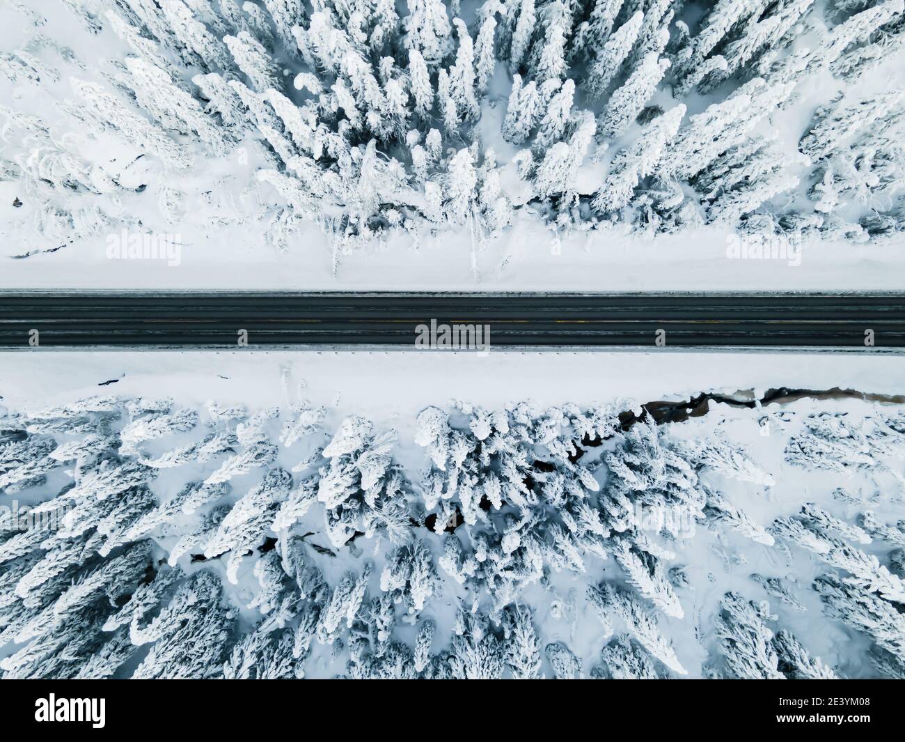 Highway cutting through a frozen snow covered forest. Birds eye view. Stock Photo