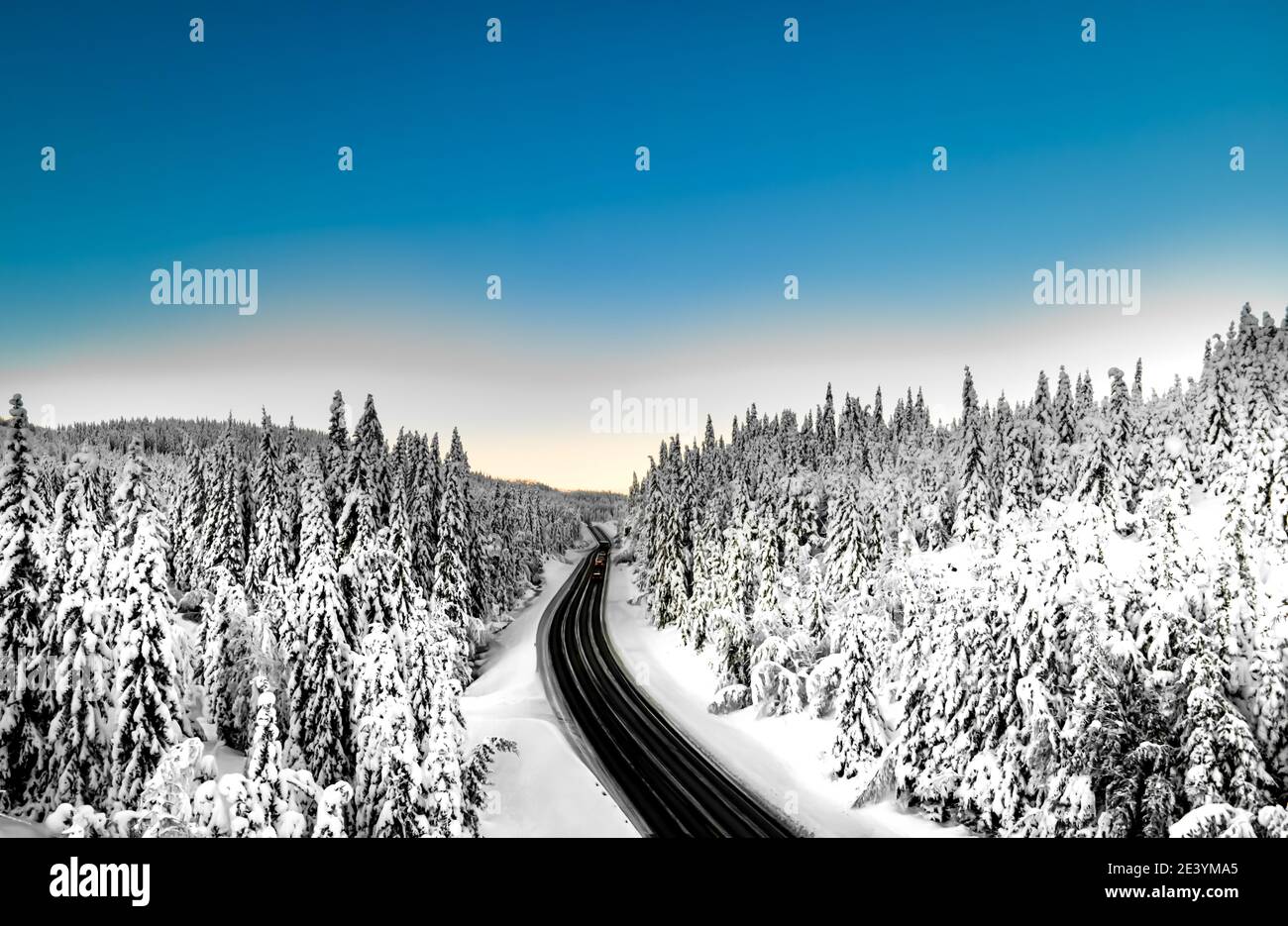 Highway with cars driving through a mountain pass with snow covered trees. Stock Photo