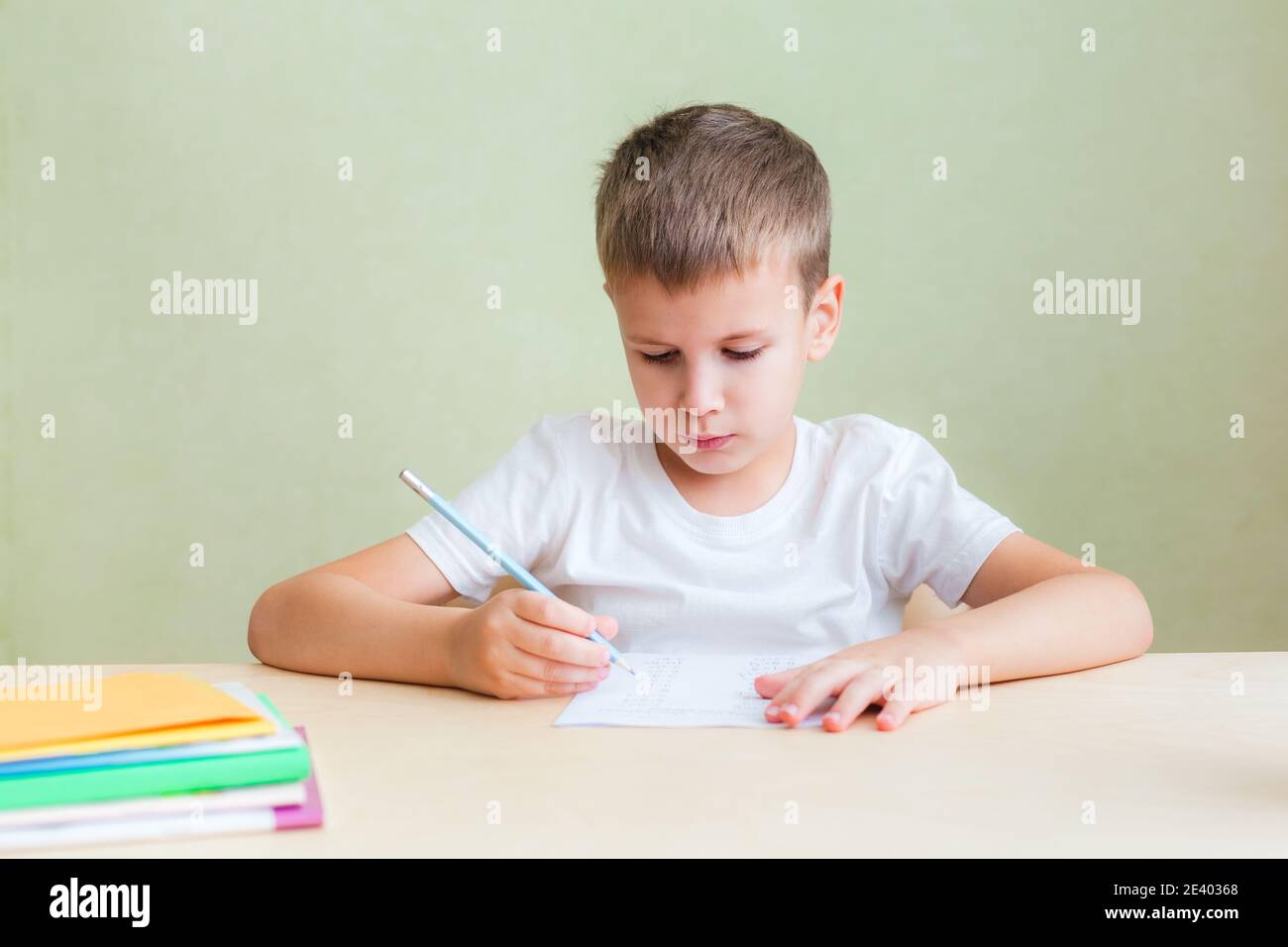 Cute child boy sits at desk in room and does written assignment in notebook Stock Photo