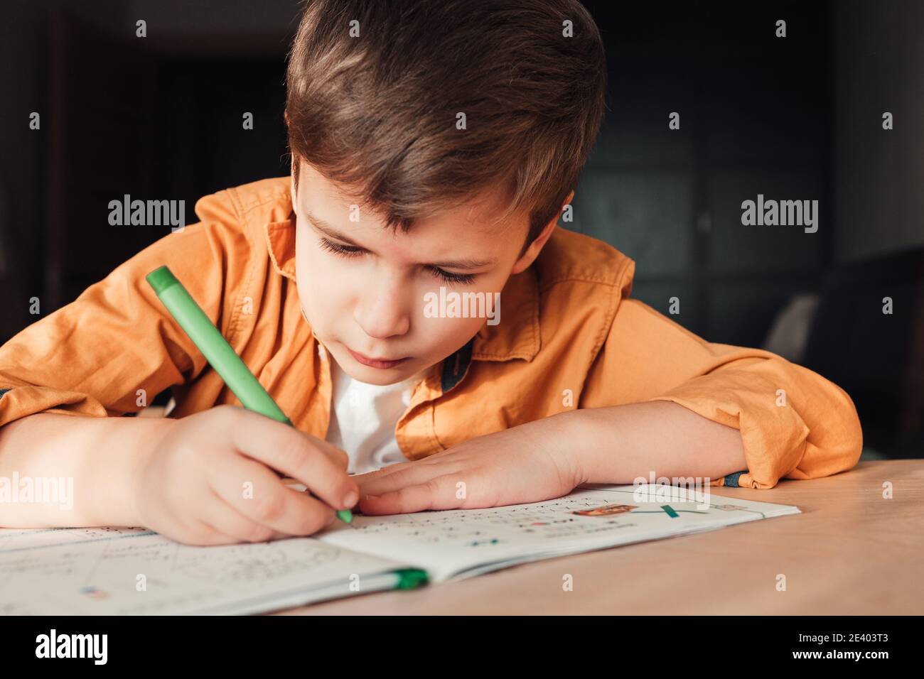 Cute 7 years old child doing his homework sitting by desk. Boy writing in notebook. Stock Photo