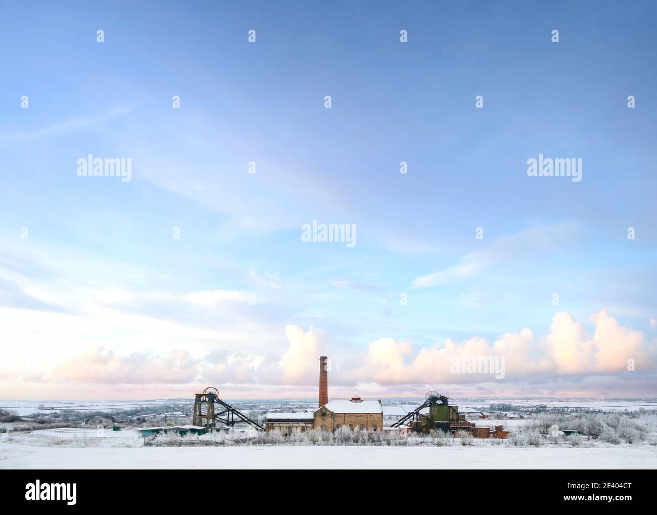 Old abandoned national coal board mine in countryside with industry engine house winding wheel snowfall Christmas winter snow scene landscape Pleasley Stock Photo