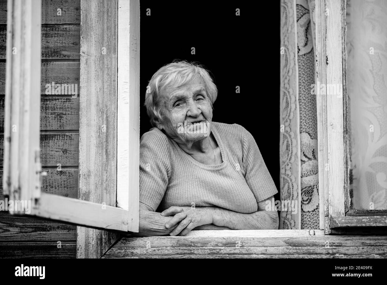An elderly woman sitting and looking out the window. Black and white photo. Stock Photo
