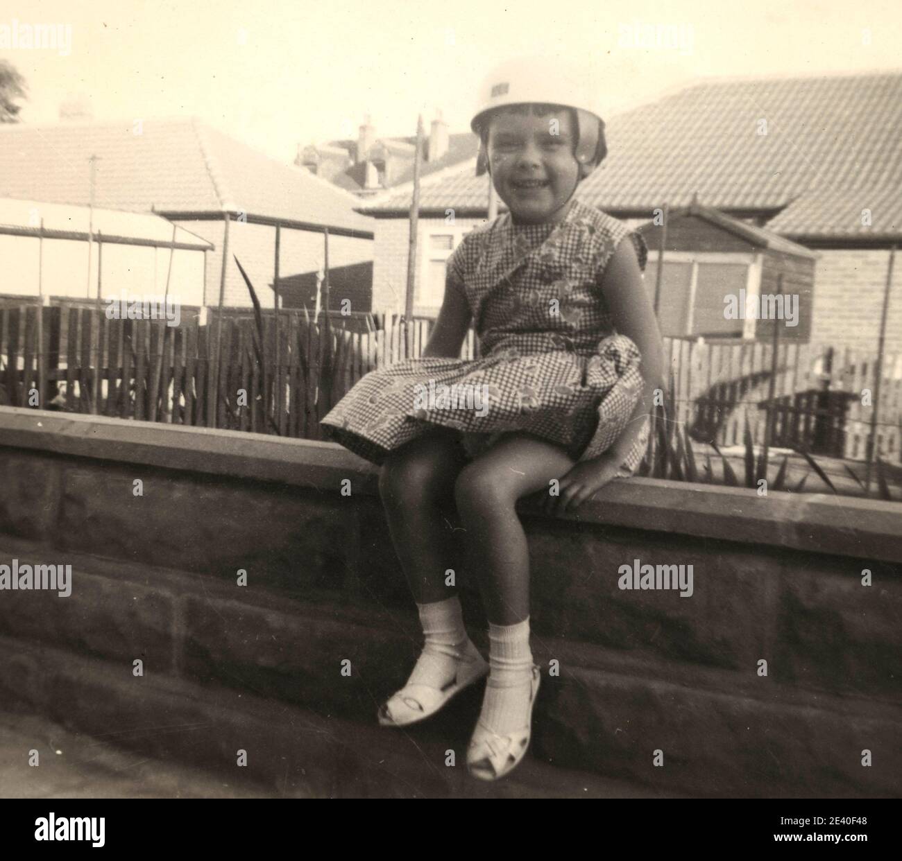 Girl wearing a dress and crash helmet sitting on a wall Stock Photo