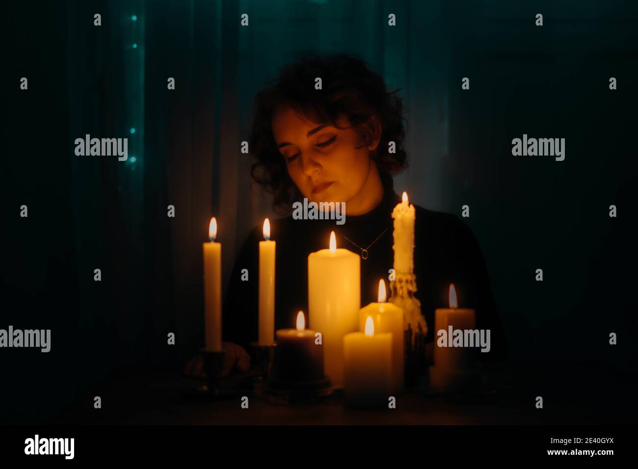 Female with closed eyes sitting near burning candles in a dark room