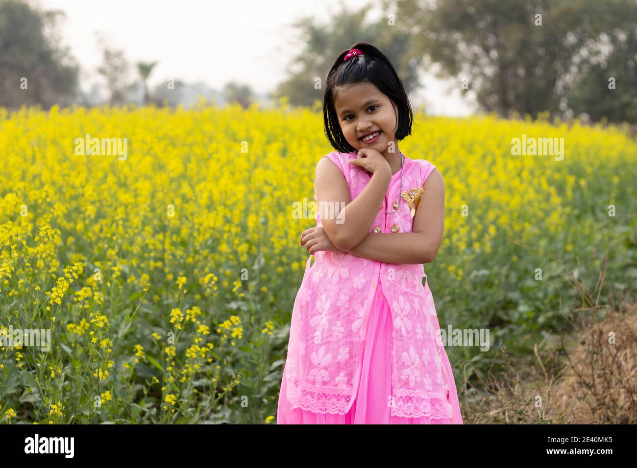 a pretty indian girl child in pink dress posing with smiling face near yellow mustard flower field Stock Photo