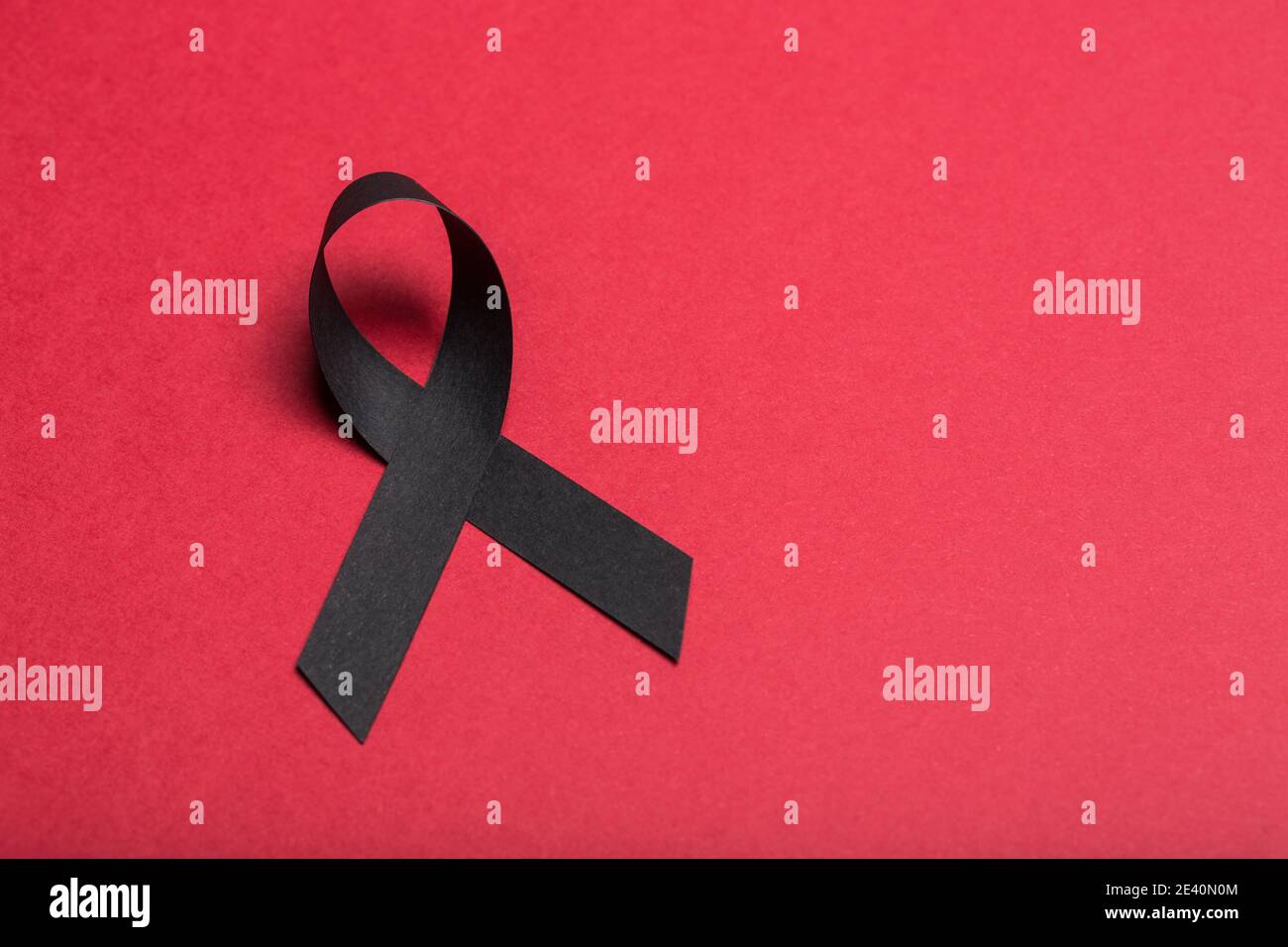 Black handmade awareness paper ribbon on red background. Stock Photo