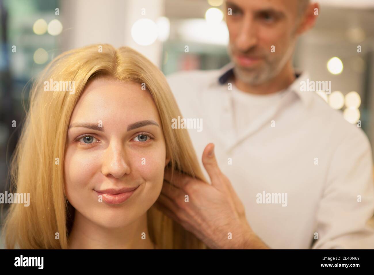 Cropped close up of a young lovely woman smiling, professional hairdresser examining her hair before haircut. Attractive female client at beauty salon Stock Photo
