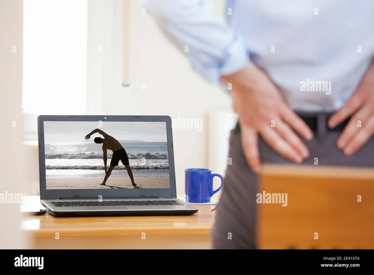 Businessman with backache standing in front of laptop while working from home - Same model on the screen and in the foreground Stock Photo