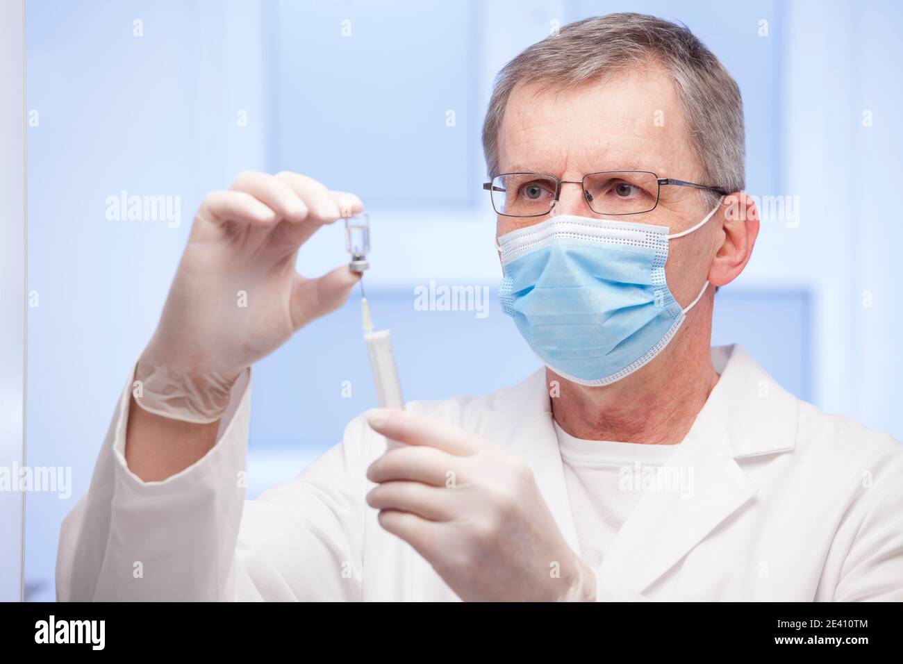 Doctor with medical mask preparing a syringe for vaccination against covid-19 - focus on the face Stock Photo