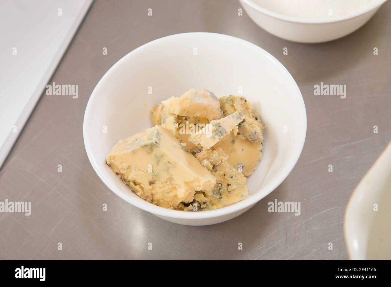Delicious blue cheese in a white ceramic bowl. It is located on a metal surface. Close-up. Stock Photo