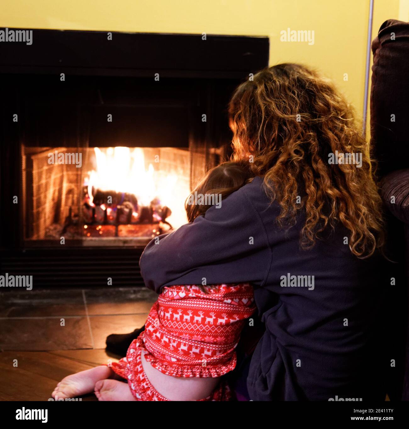 A mother and daughter cuddling each other in front of the fire in winter Stock Photo