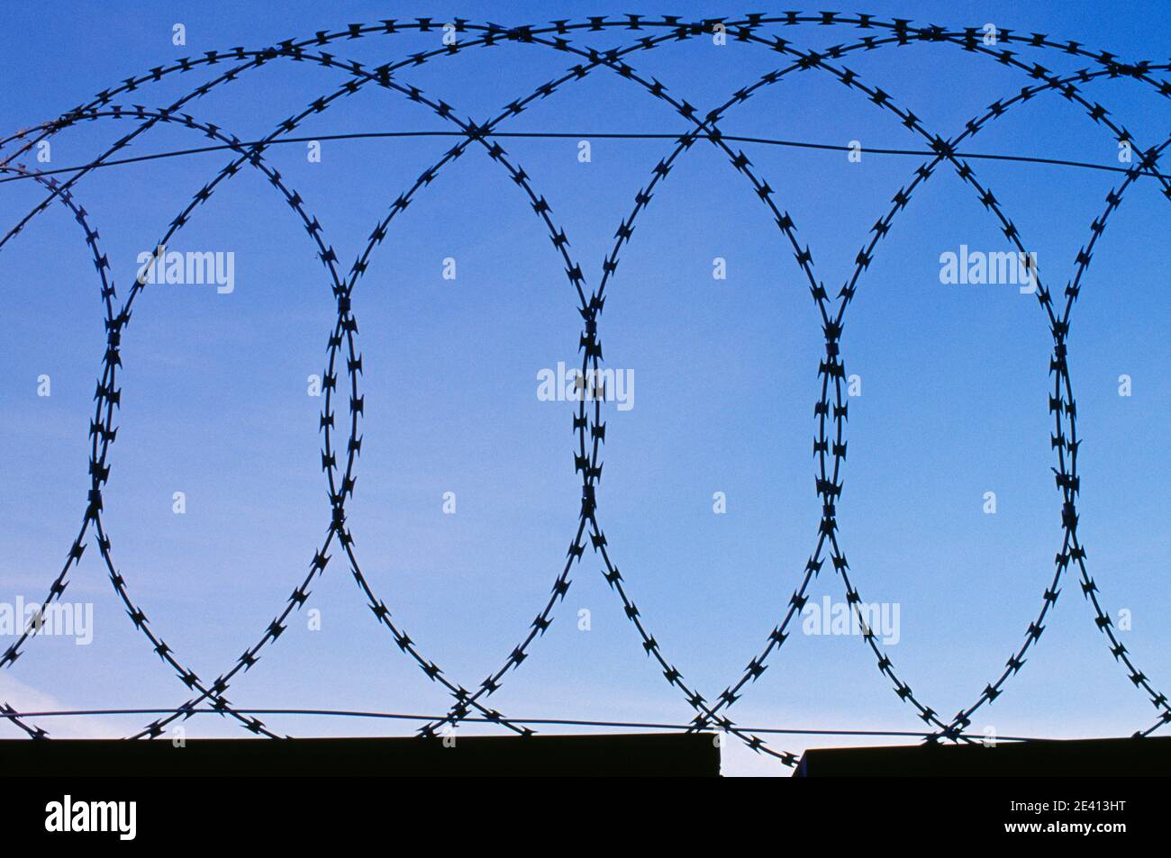 Razor wire surrounding the gasometers, loops of wire seen against blue ...