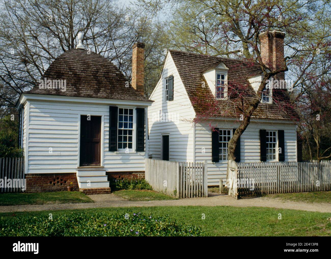 Small cape cod style house with chimney and garden enclosed by picket