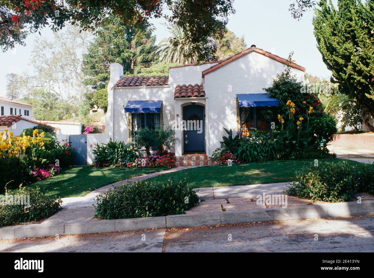 Small 1920s whitewashed single storey house, blue awnings, tiled roof, canna lilies, santa