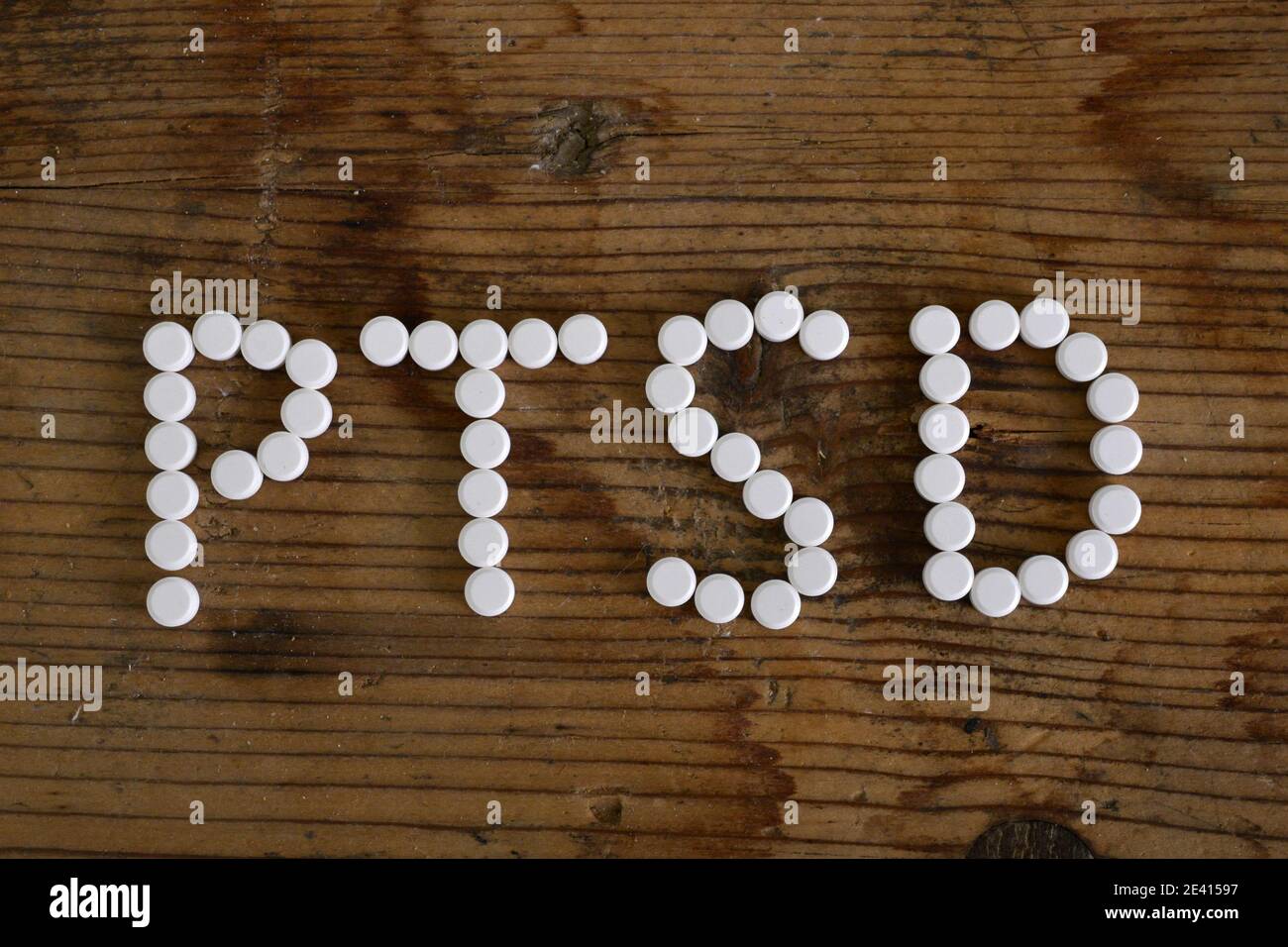 text Ptsd. writing with pills on wooden table . Concept meaning Post Traumatic Stress Disorder Mental Illness Trauma Fear Depression. Stock Photo