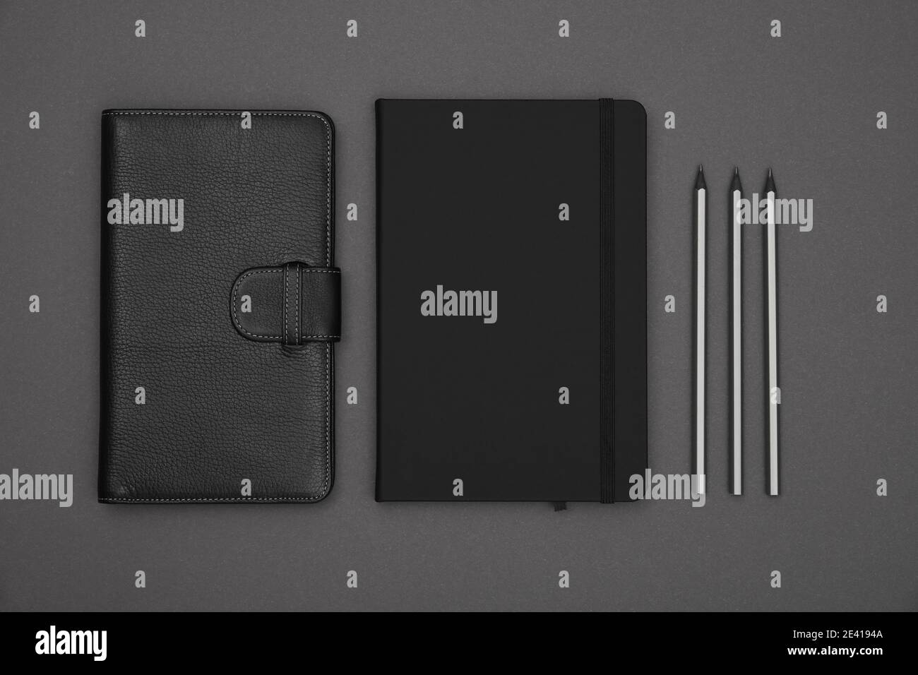 Close up two closed black leather cover notebooks and pencils over grey paper background, flat lay, directly above Stock Photo