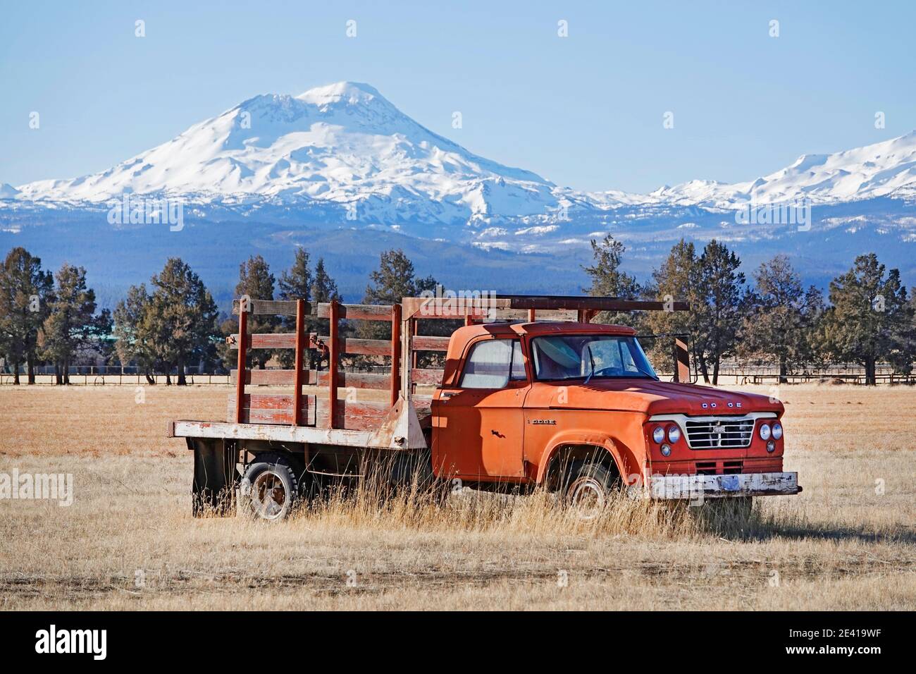 An ancient red farm truck in a field below South Sisters Peak in the Oregon Cascade Mountains near the small resort town of Sisters, Oregon. Stock Photo