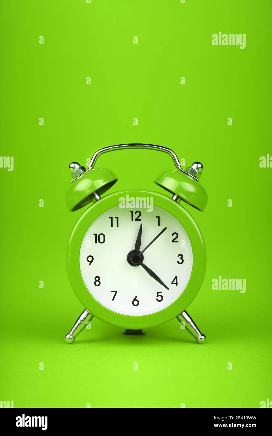 Close up one small green metal twin bell retro alarm clock over fresh green color paper background with copy space, low angle front view Stock Photo